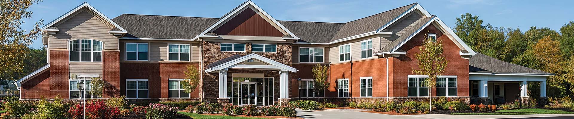 A beautifully designed assisted living facility featuring brick and stone exterior elements, surrounded by vibrant landscaping and greenery.