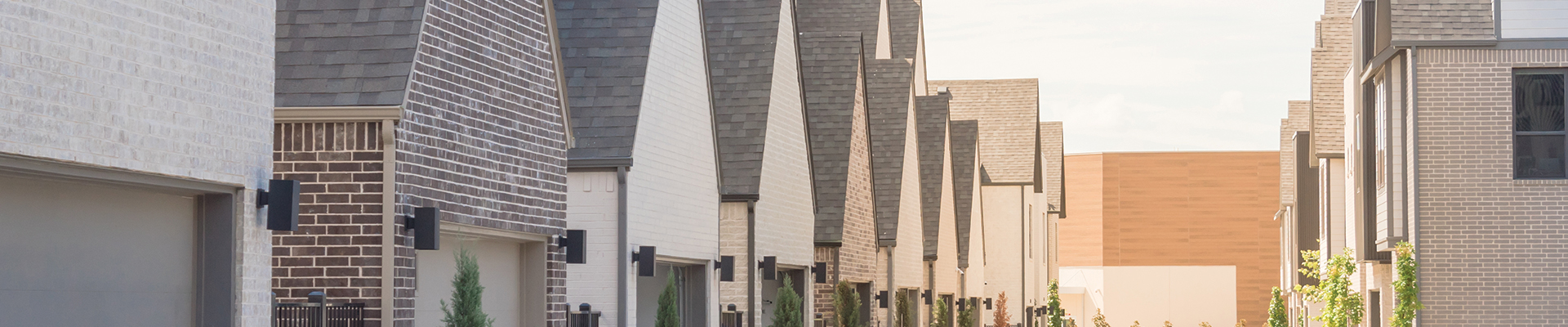 Modern row of multifamily homes with brick facades, uniform pitched roofs, and landscaped entrances, creating a cohesive and contemporary neighborhood feel.